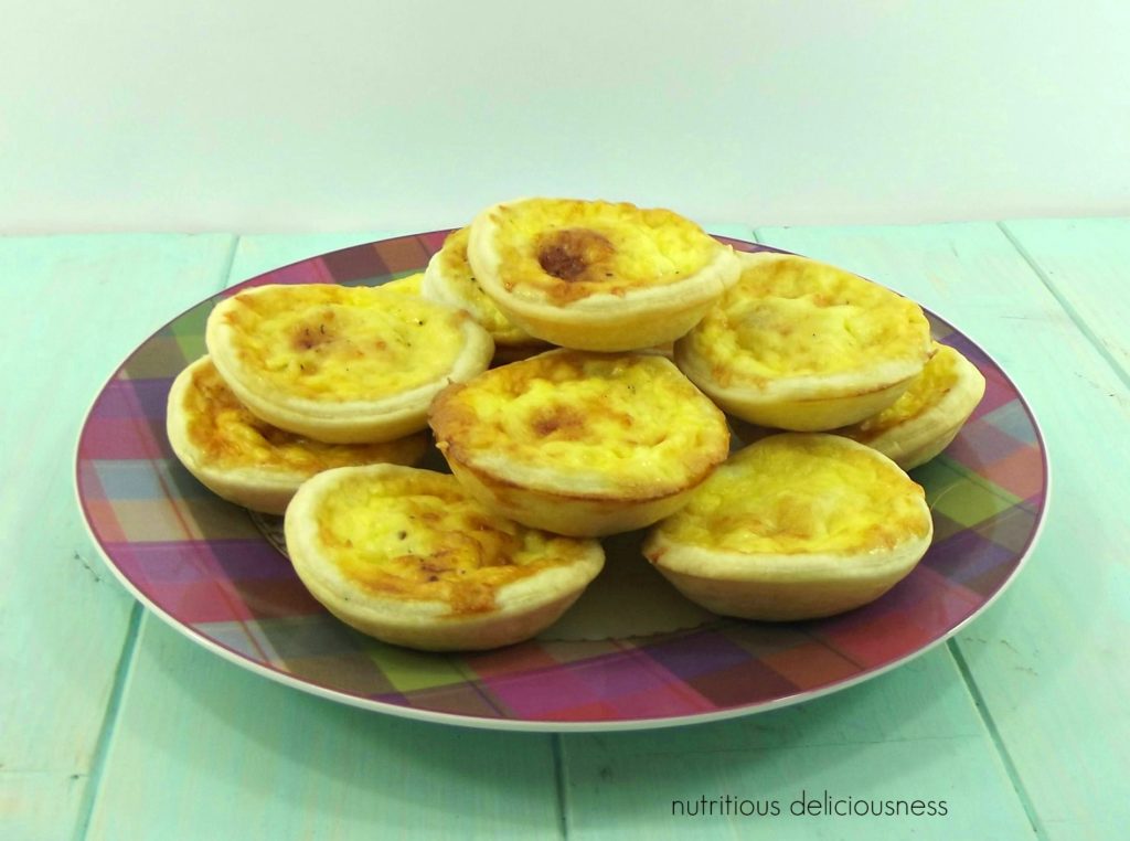 Mini Gruyere Quiches on a tartan patterned plate on an aqua wooden board.