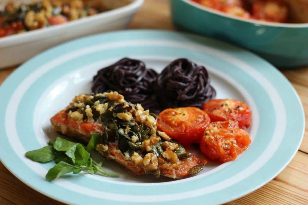 Roasted salmon with roasted tomatoes and black soba noodles on a blue and white striped plate