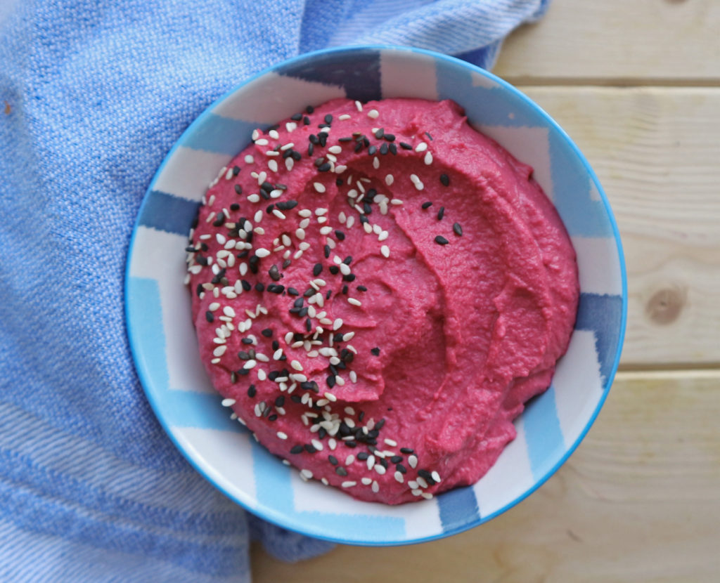 Roasted Beetroot Hummus in blue and white bowl on wooden board with a blue tea towel.