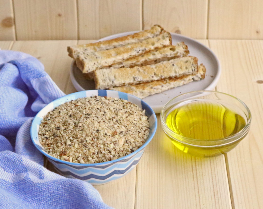 Dukkah in blue bowl with olive oil in glass bowl and bread fingers