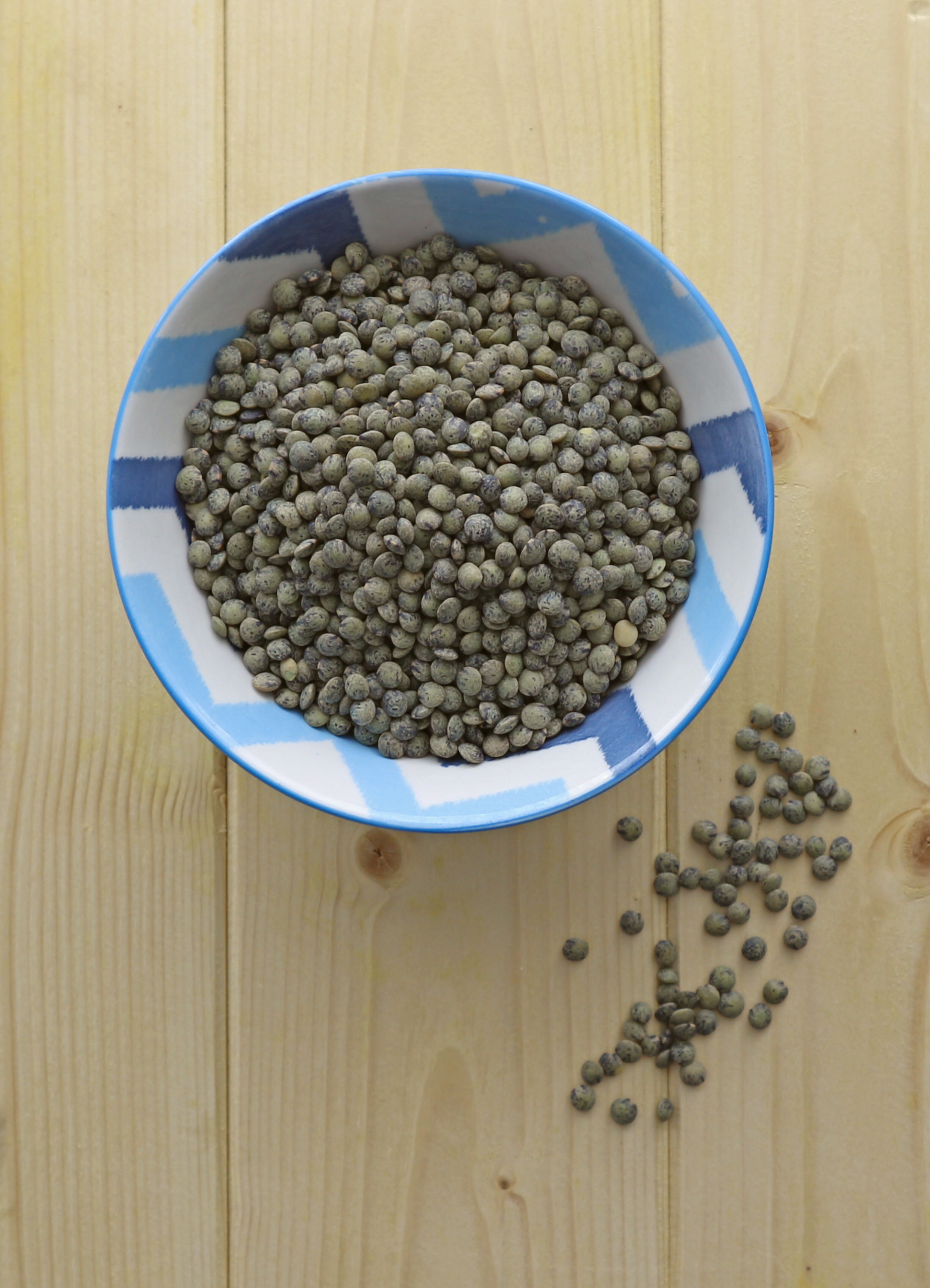 Green Lentils in a blue bowl on a wood surface.
