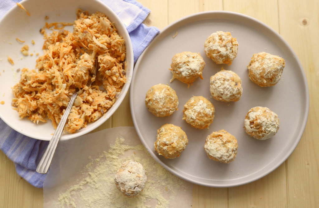 raw vegan meatballs on a cream plate with a bowl of the mixture next to it.