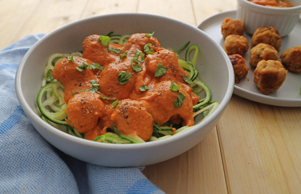 grey bowl with vegan meatballs covered with roasted tomato sauce sitting on a bed of courgetti