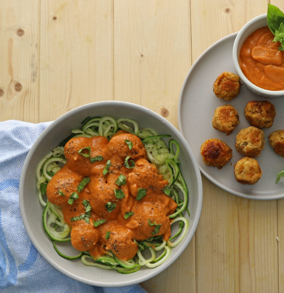 bowl of vegan meatballs covered in roasted tomato sauce and sitting on a bed of courgetti, courgette spaghetti