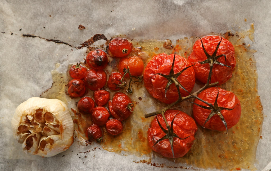 roasted large and cherry tomatoes on a baking tray with roasted large garlic bulb