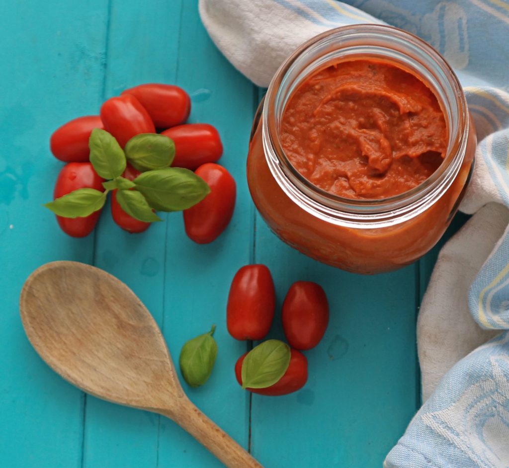 Roasted tomato sauce with fresh tomtoes and a wooden spoon on a blue board