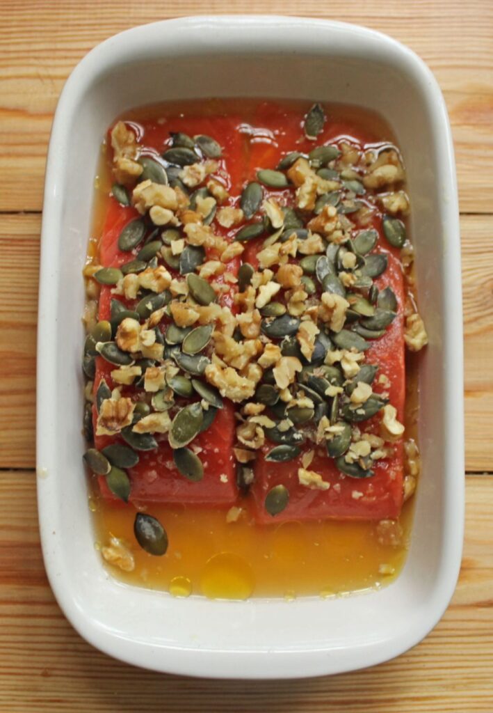 Raw salmon marinating in white dish with pumpkin seeds and walnts on top