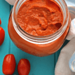 Roasted tomato sauce with fresh tomatoes and a wooden spoon on a blue board