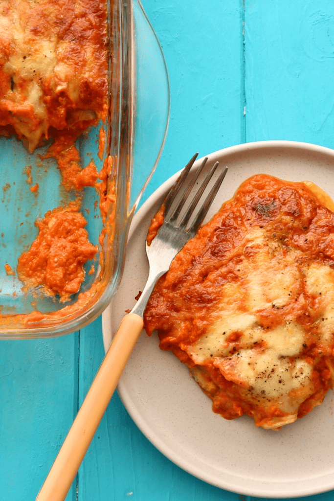 Zucchini Parmigiana slice on white plate with fork and casserole on side