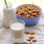 almond milk in glass and milk bottle with blue bowl filled with almonds
