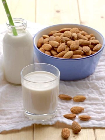 almond milk in glass and milk bottle with blue bowl filled with almonds