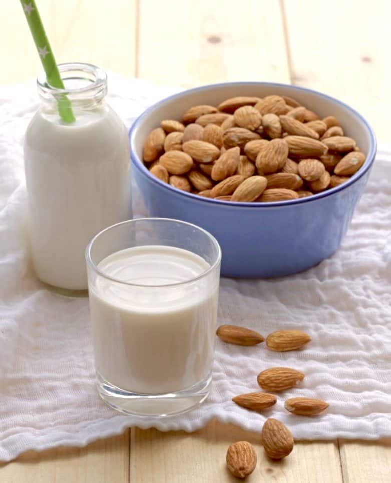 almond milk in glass and milk bottle with blue bowl filled with almonds