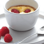 Baked Ricotta Pudding on a grey plate with 3 raspberries and a teaspoon