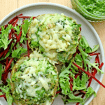 Cheesy Parsley Pesto Baked Potatoes over bed of mixed greens and open jar of pesto in background