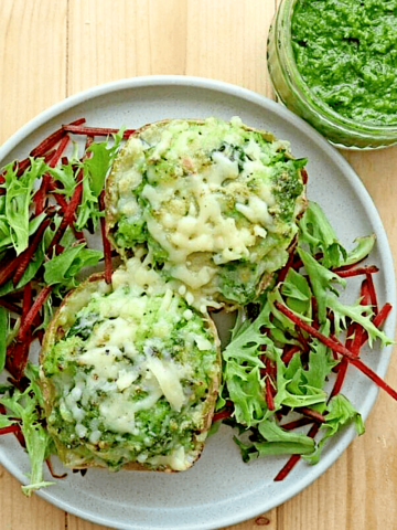 Cheesy Parsley Pesto Baked Potatoes over bed of mixed greens and open jar of pesto in background