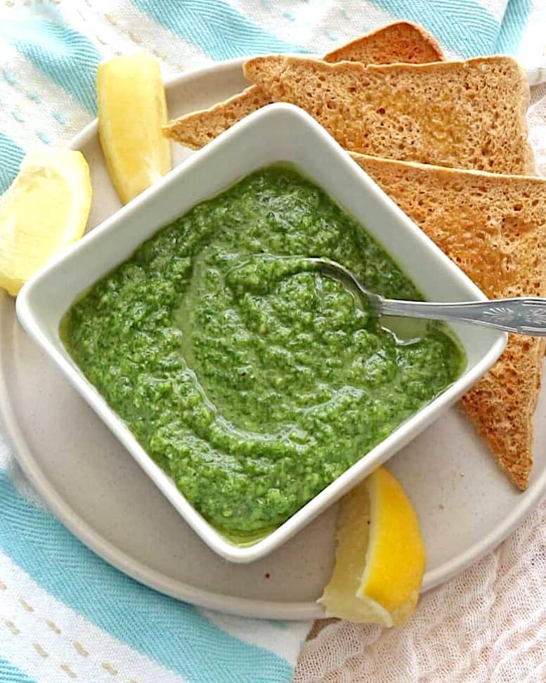 Parsley Pesto with Almonds in square white bowl with lemons and toast in background