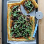 Puff Pastry Tart filled with sweet potato, red onions, mushrooms and mozzarella cheese on a baking tray that is on a wooden board.