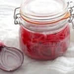 Pink pickled onions in a sealed glass jar with one whole red onion and half a red onion.