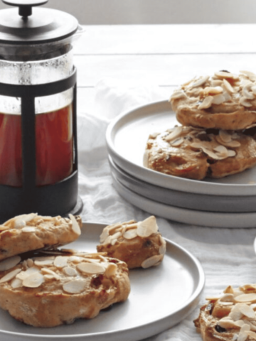 Two Stollen Pastries on a grey plate with one on the side. Plus a pile of plates with 3 Stollen Pastries on. Cafetiere full of fresh coffee and a coffee cup and saucer with black coffee.