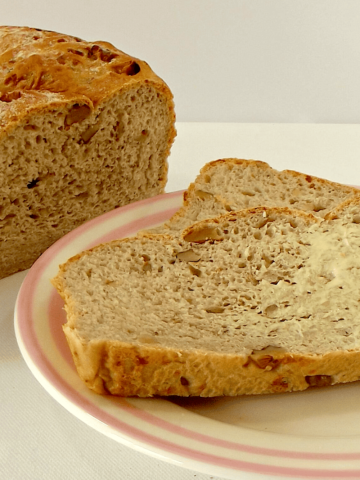 Walnut and Gruyere loaf with a buttered slice on a plate.