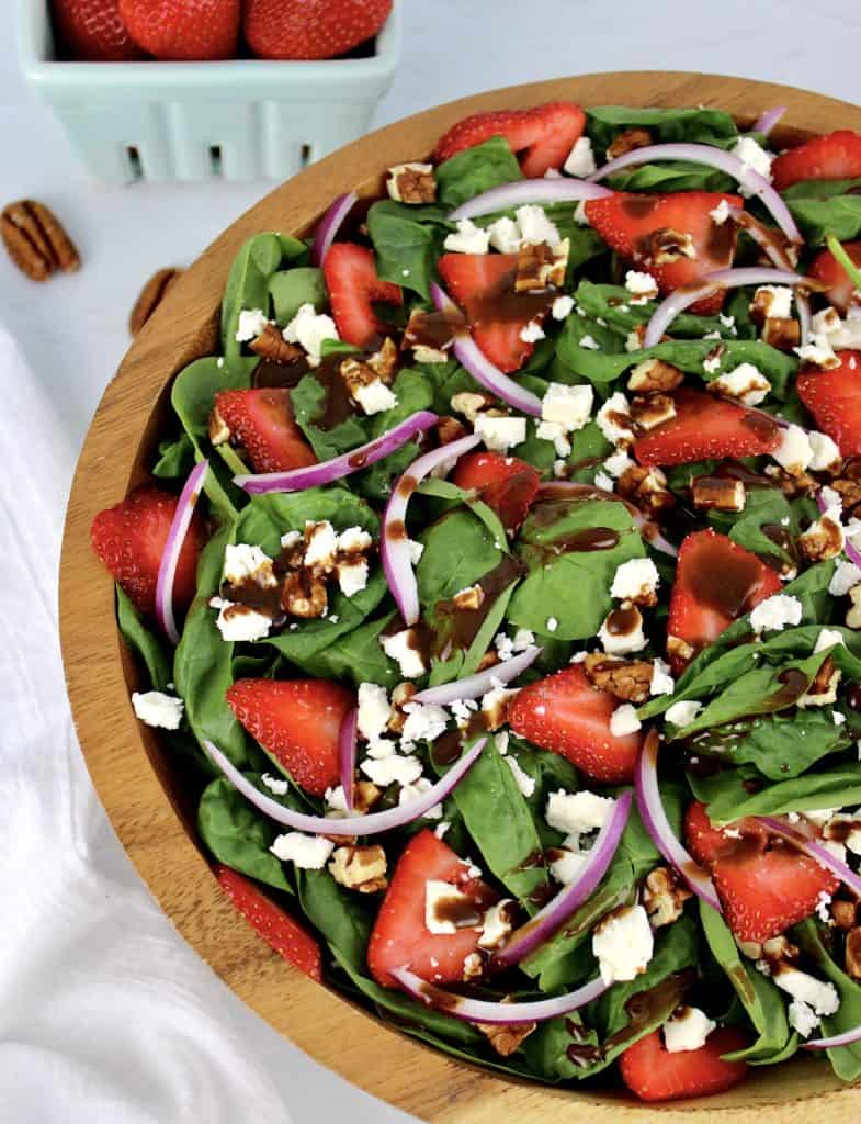 Strawberry Spinach Salad with Balsamic Vinaigrette in wooden bowl strawberries in background