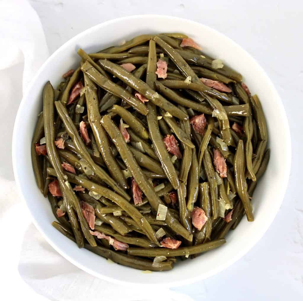 overhead view of green beans in white bowl with chunks of ham and onion