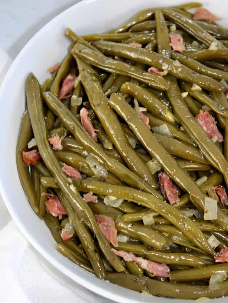 overhead view of cooked green beans with chunks of ham in white bowl