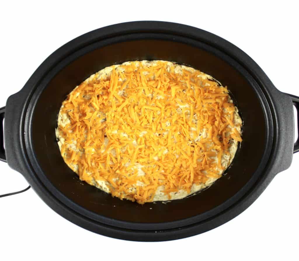 creamy chicken with shredded cheddar on top in slow cooker