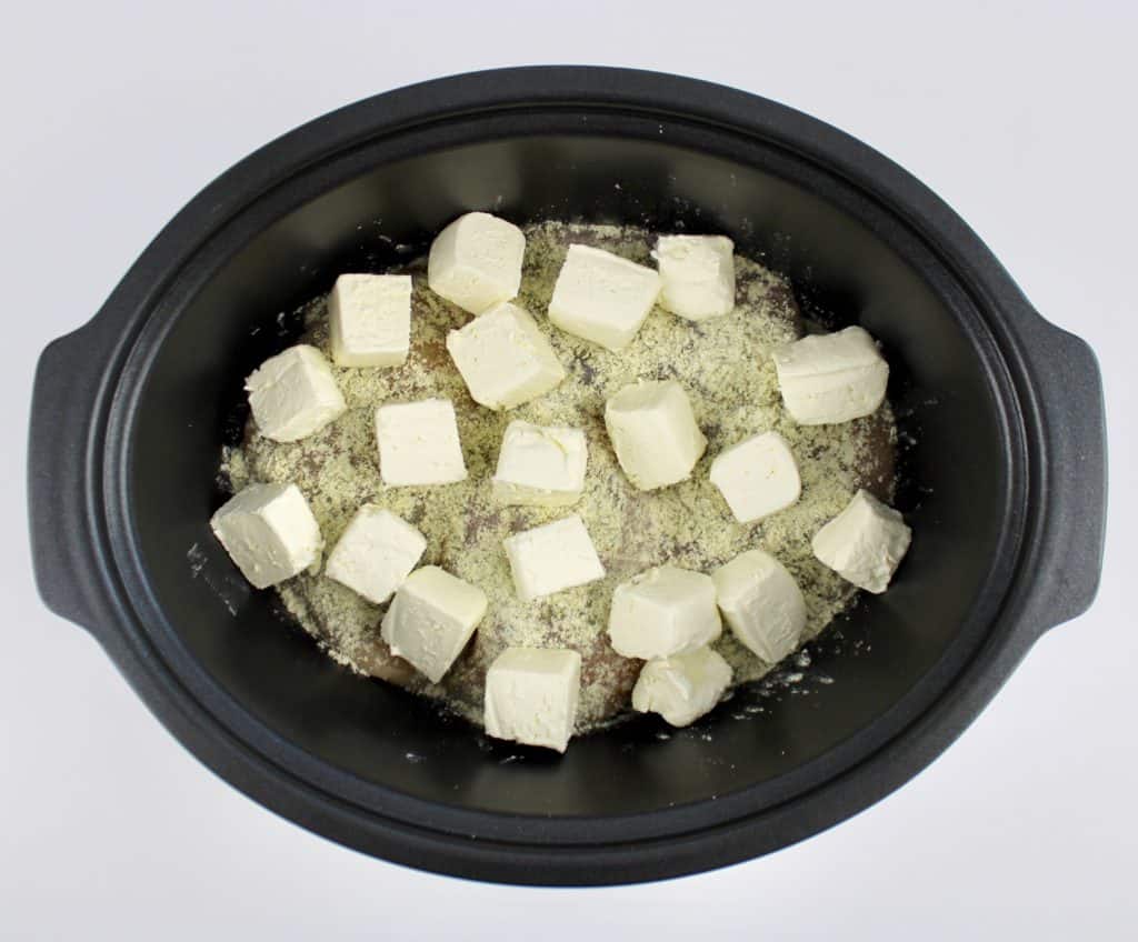 ranch chicken in slow cooker with cubes of cream cheese on top