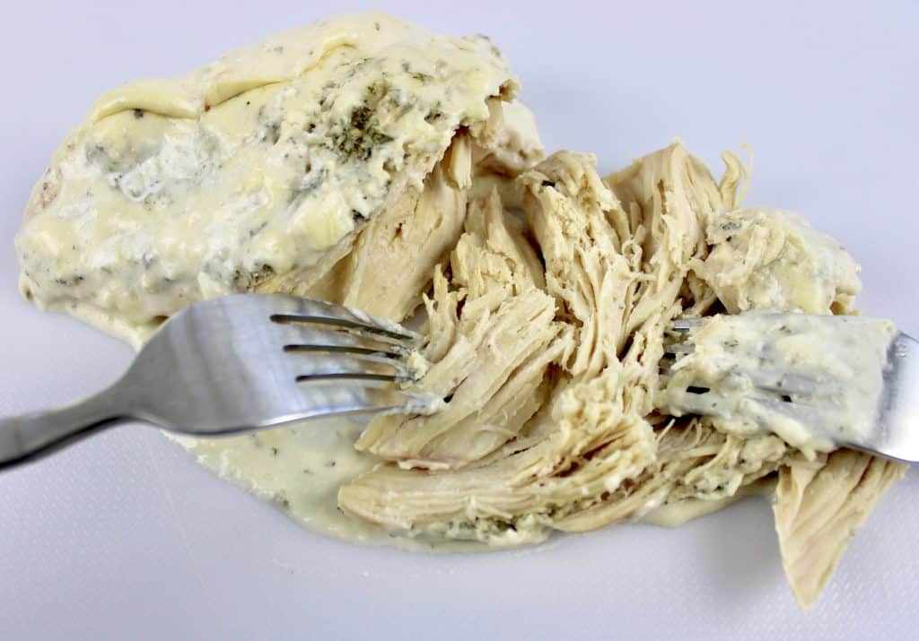 shredding chicken with 2 forks on white cutting board
