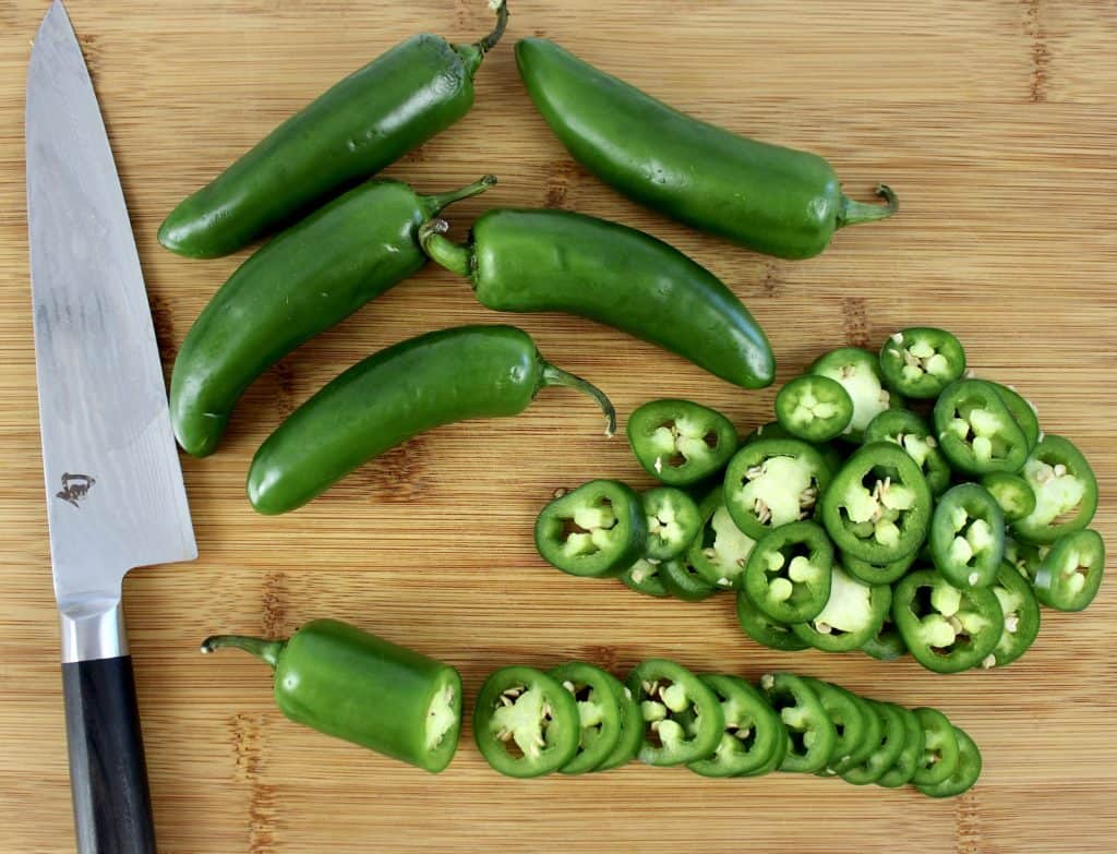 jalapeno peppers on cutting board with some sliced and knife on the side