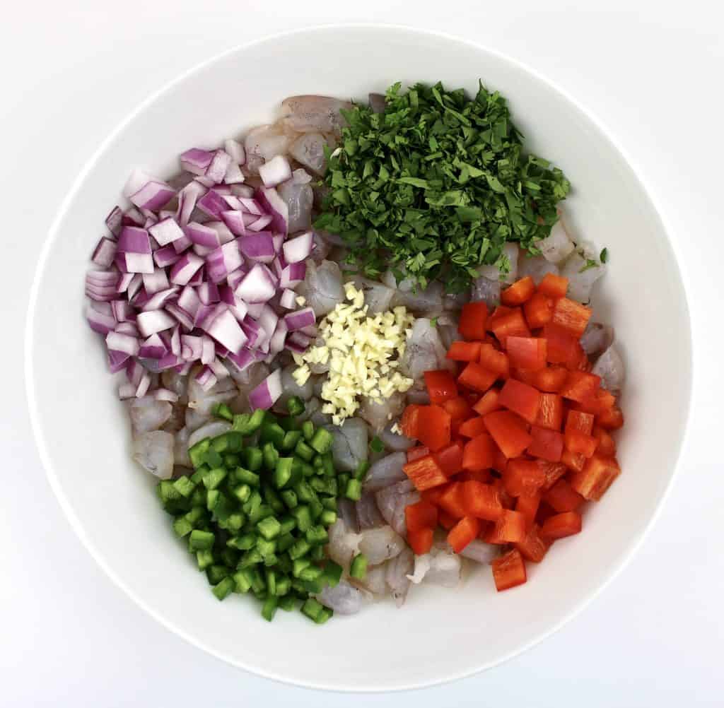 raw chopped shrimp cilantro red onion garlic and red bell pepper in white bowl