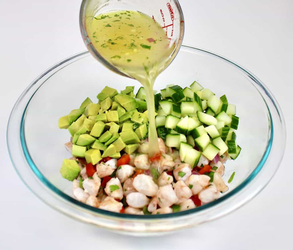 lemon dressing being poured over chopped veggies in white bowl