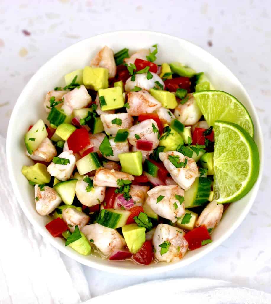 Shrimp Ceviche in white bowl with chopped veggies 2 lime slices