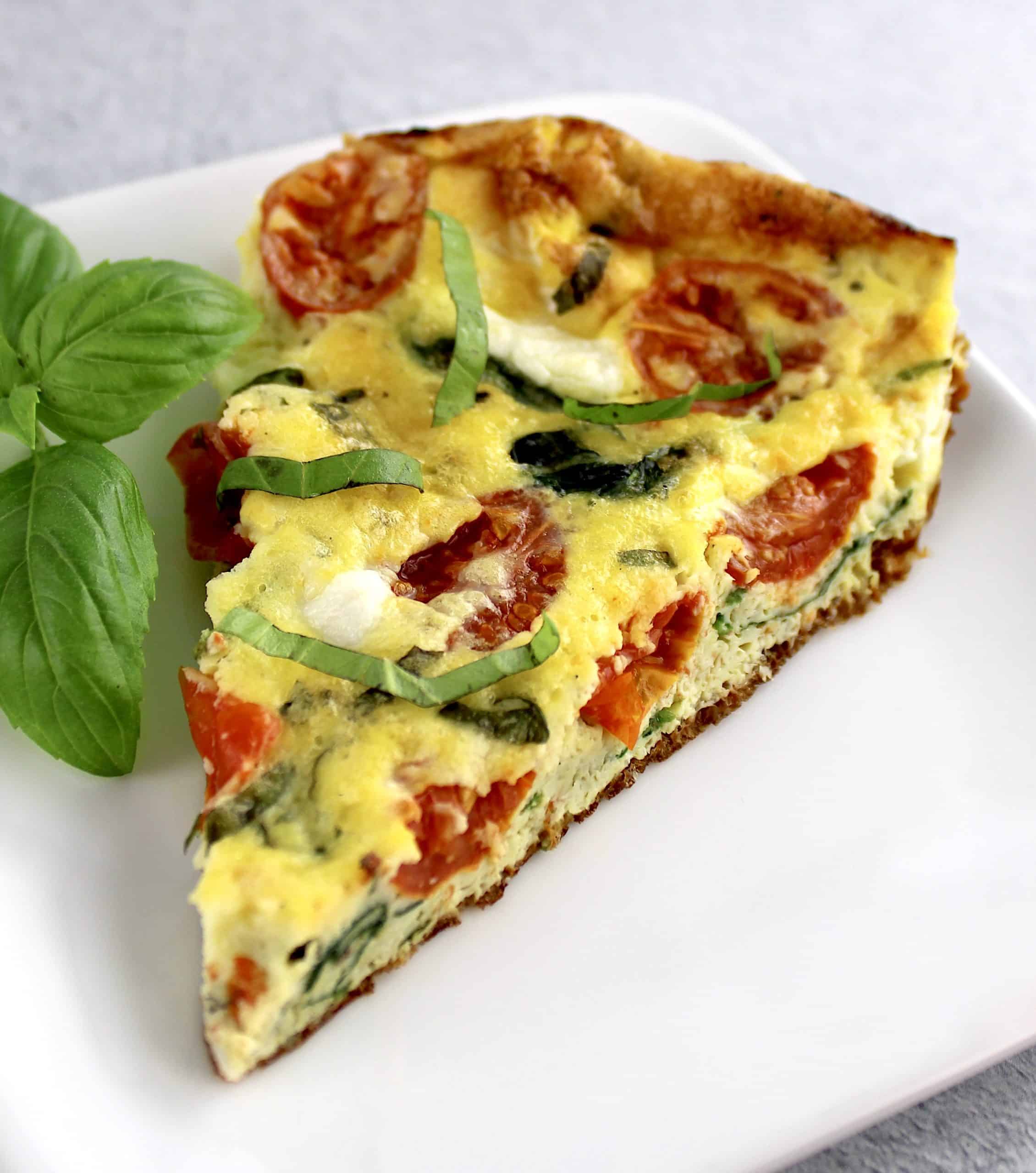 slice of caprese frittata on white plate with basil garnish