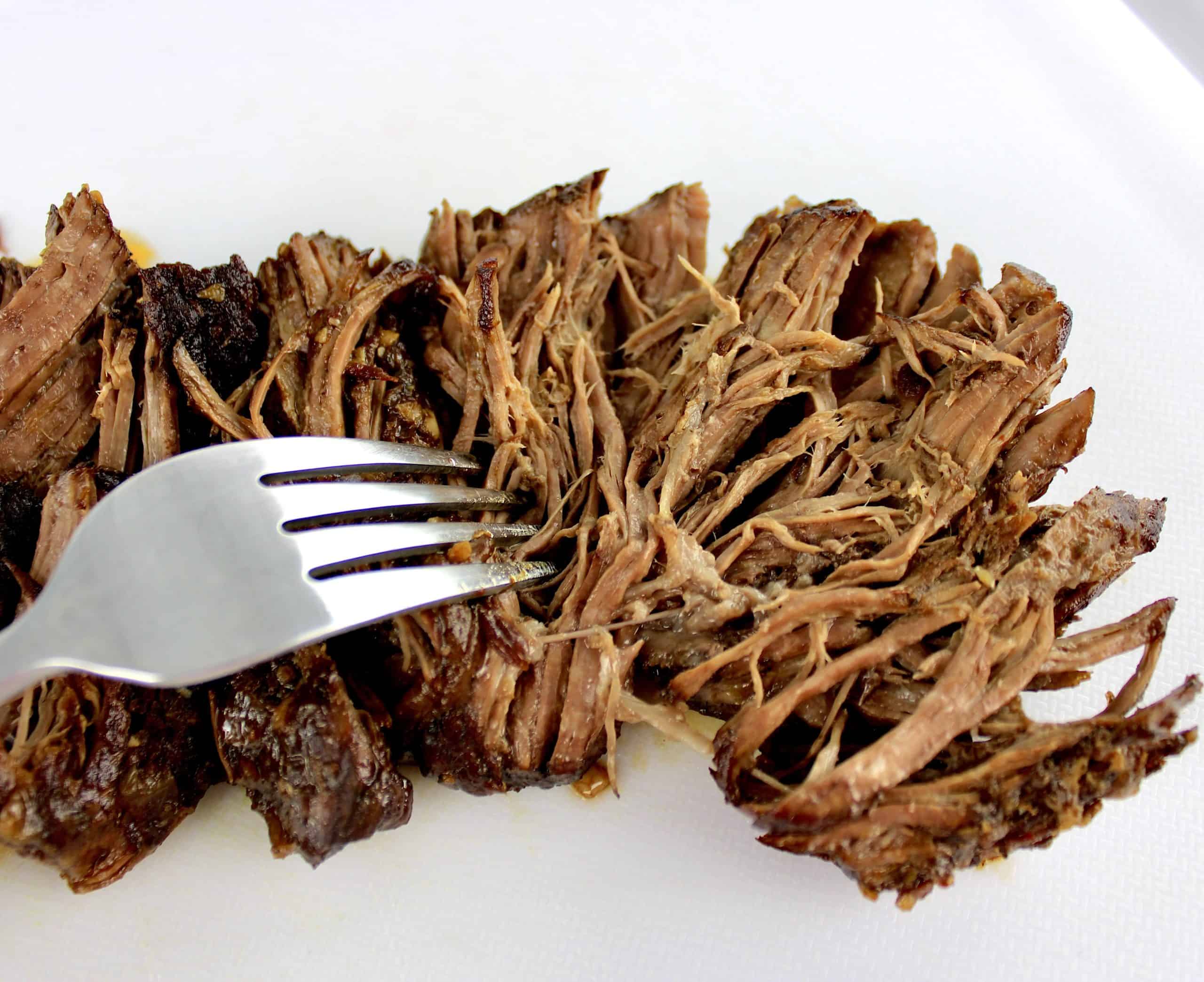 fork shredding beef on white cutting board