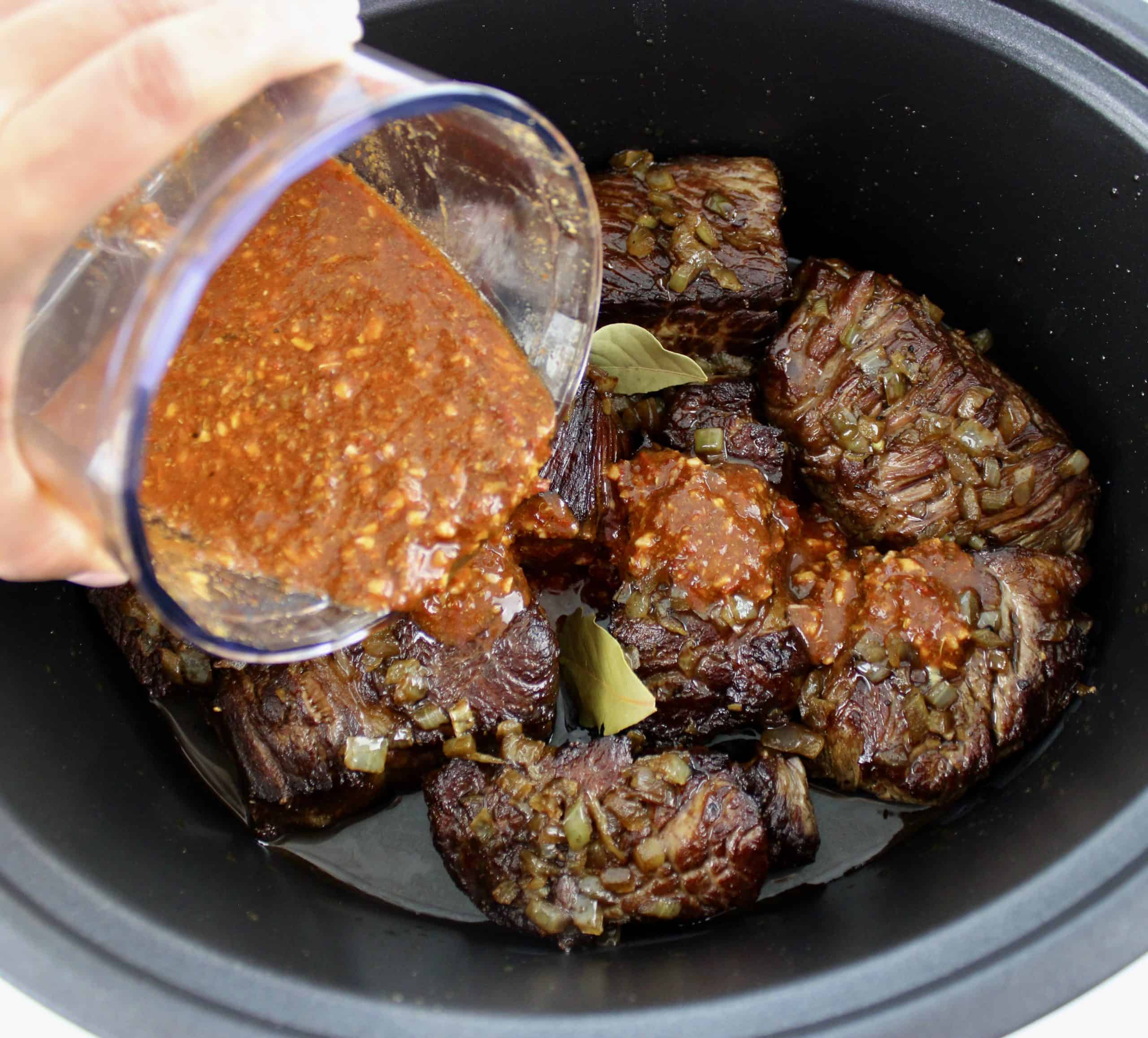 chipotle sauce being poured over chunks of chuck roast in slow cooker