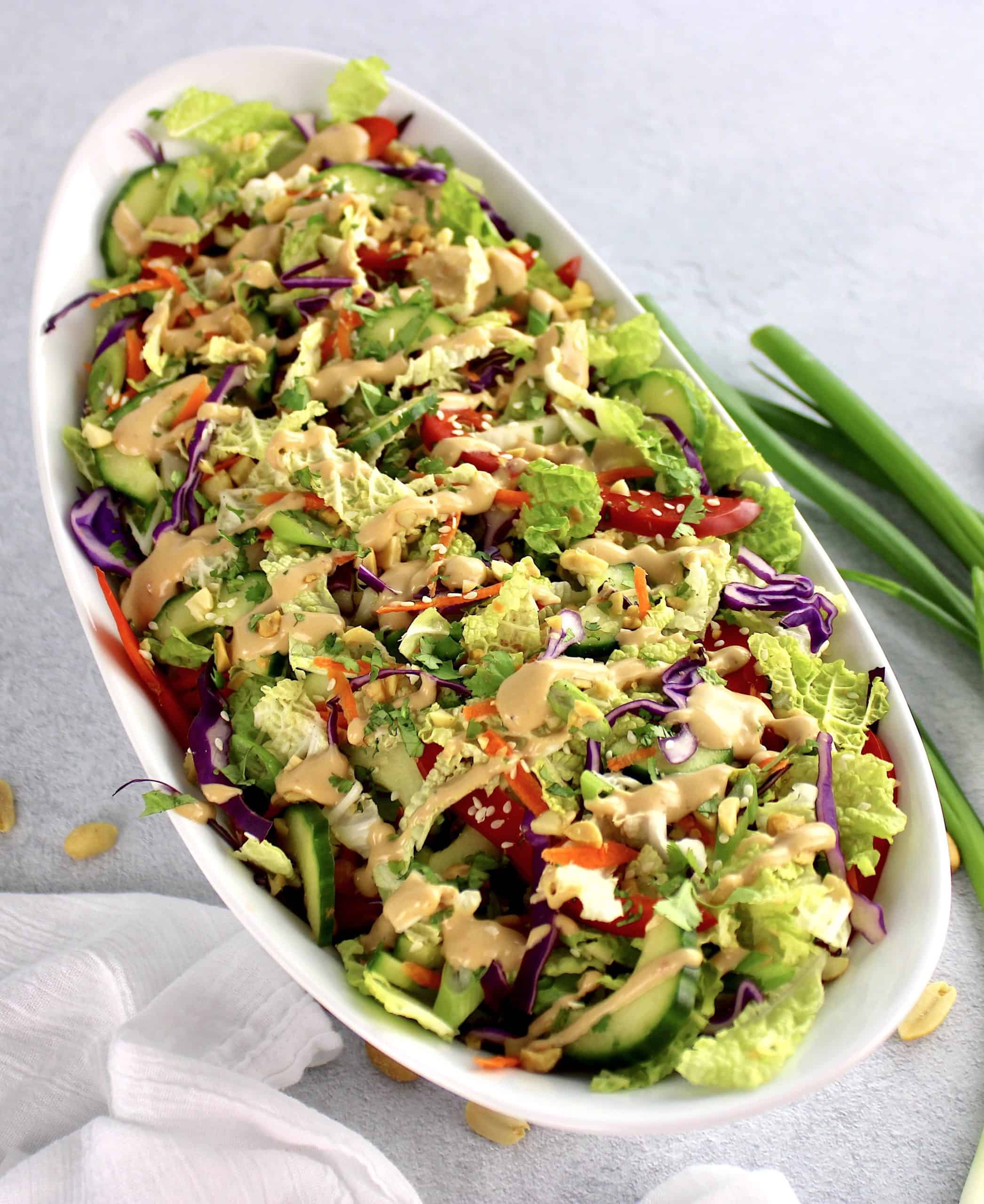 Thai Crunch Salad with Peanut Dressing in white bowl scallions in background
