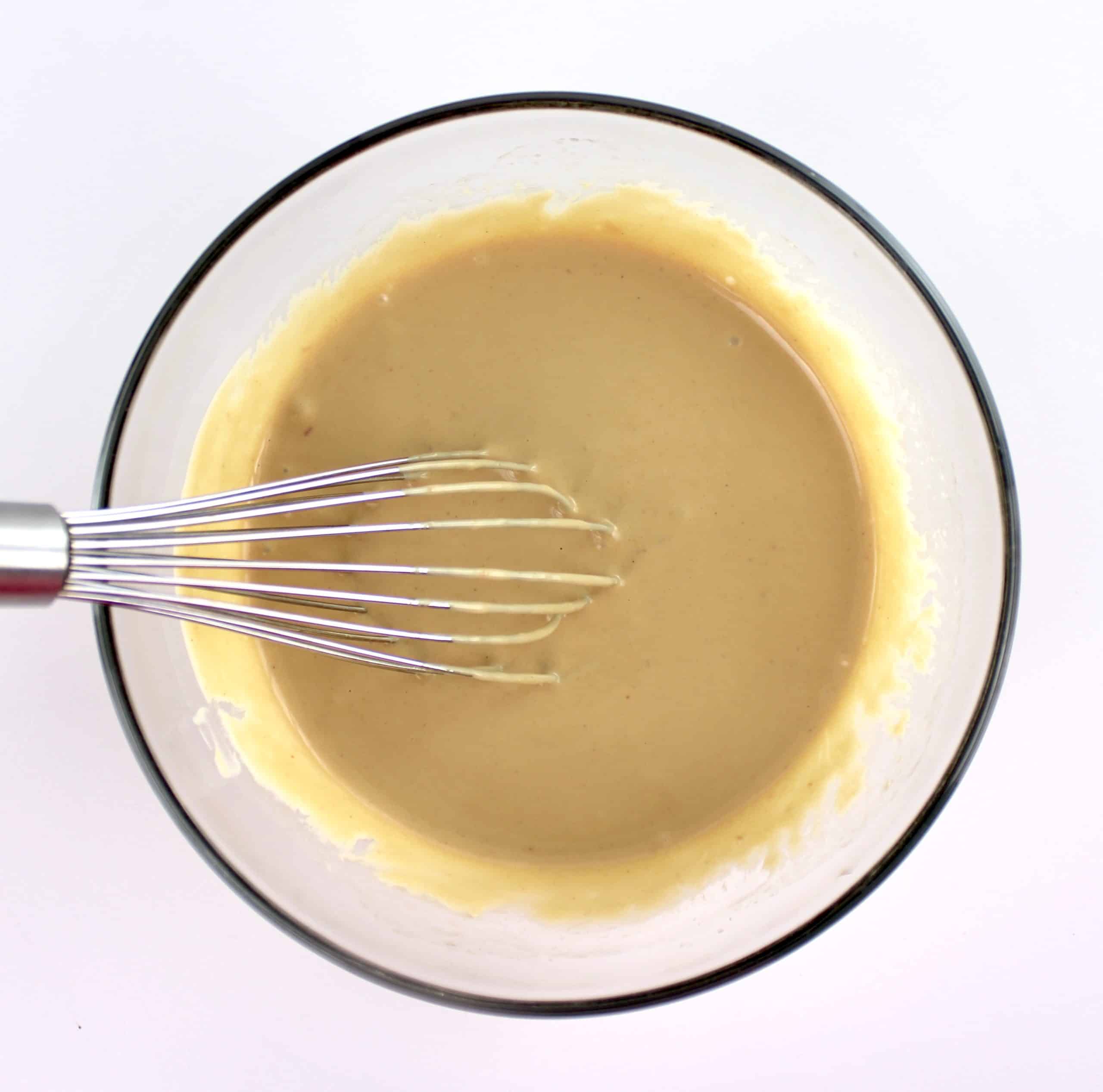 thai peanut dressing in glass bowl with whisk