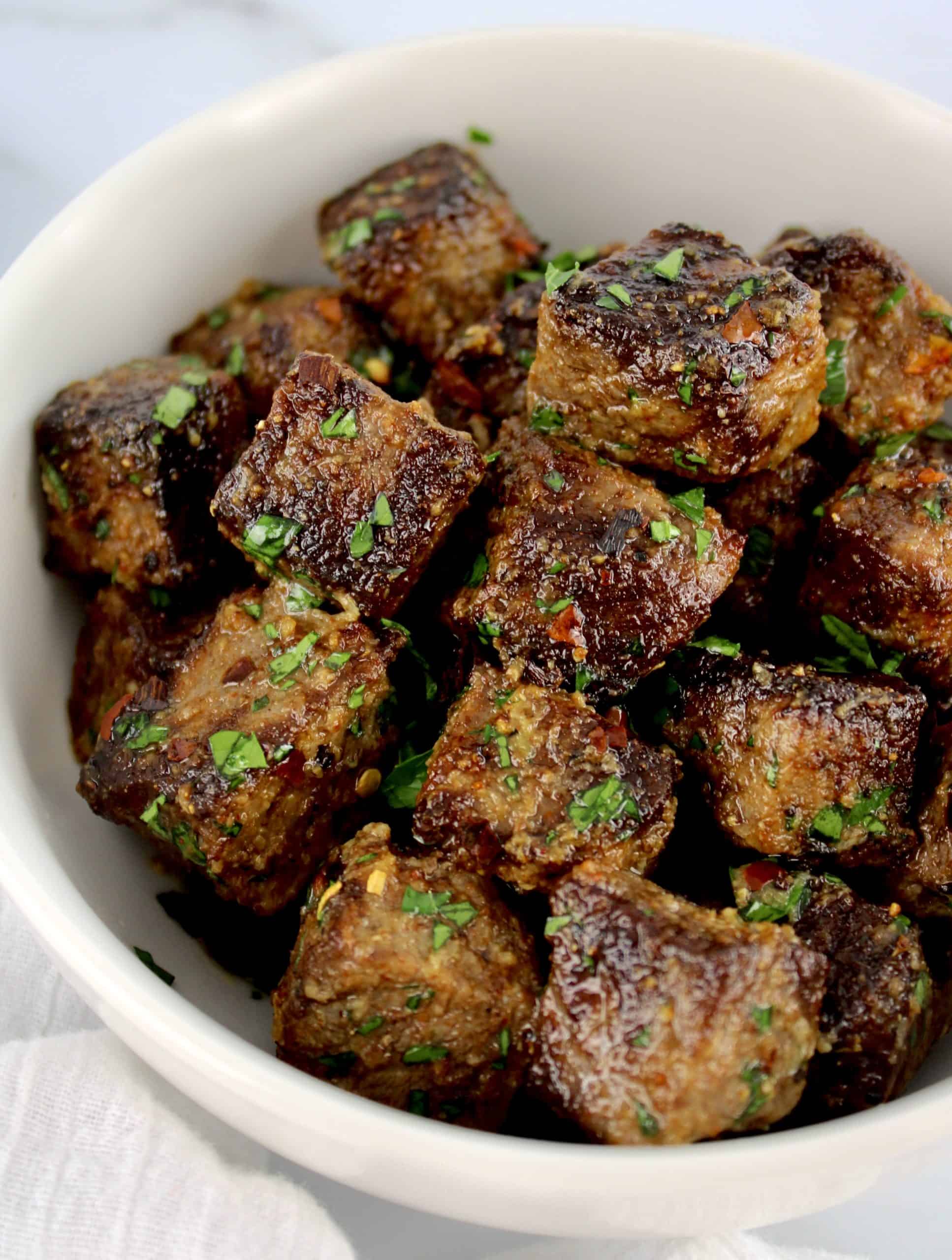 Air Fryer Steak Bites in white bowl with chopped parsley garnish