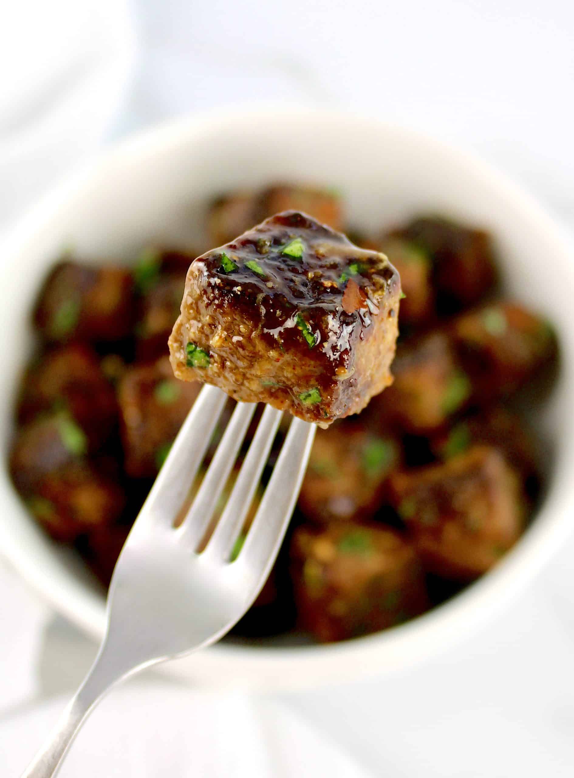 steak bite on the end of a fork with bowl of steak bites in background