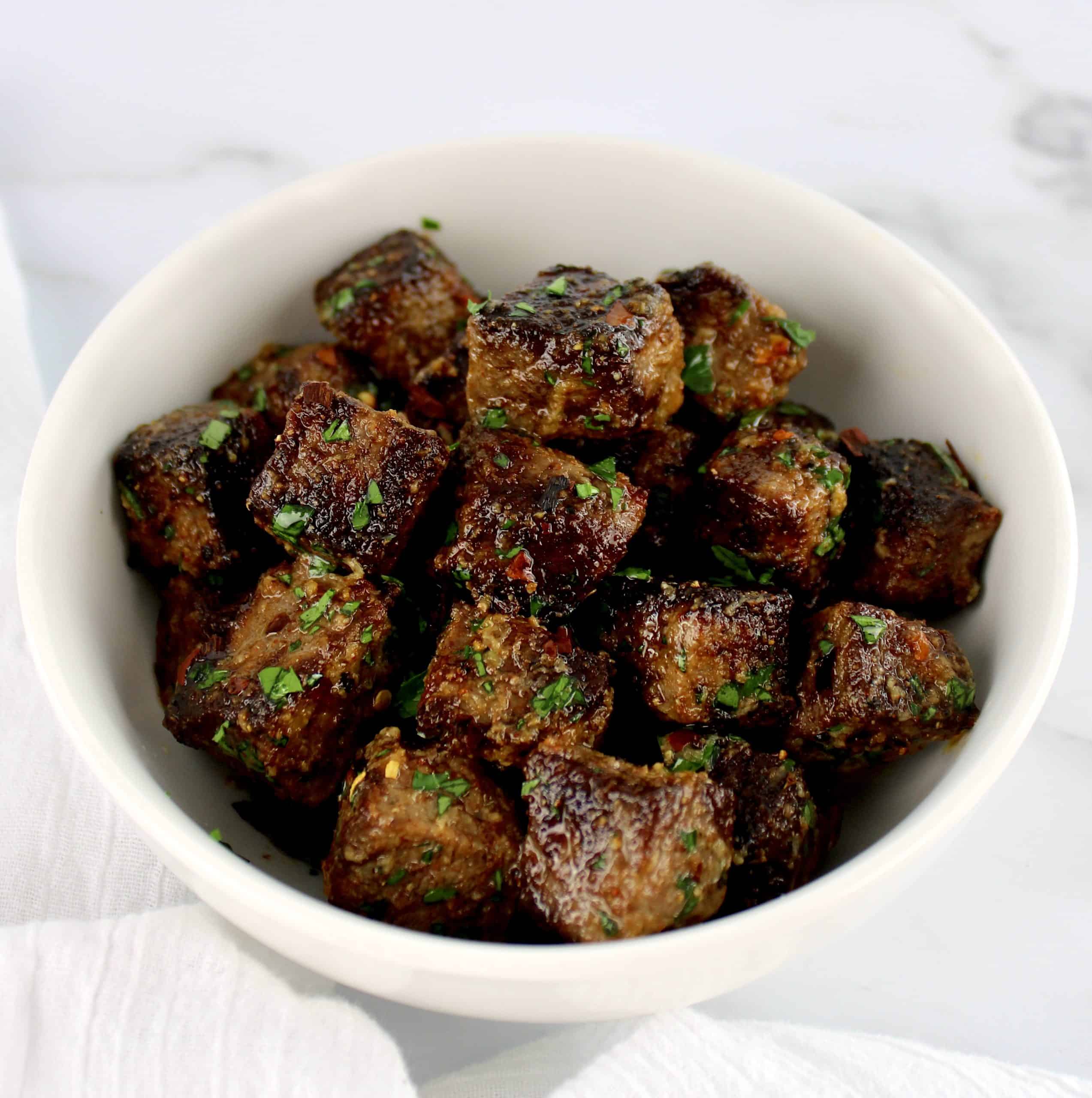 Air Fryer Steak Bites tossed in garlic butter sauce in white bowl