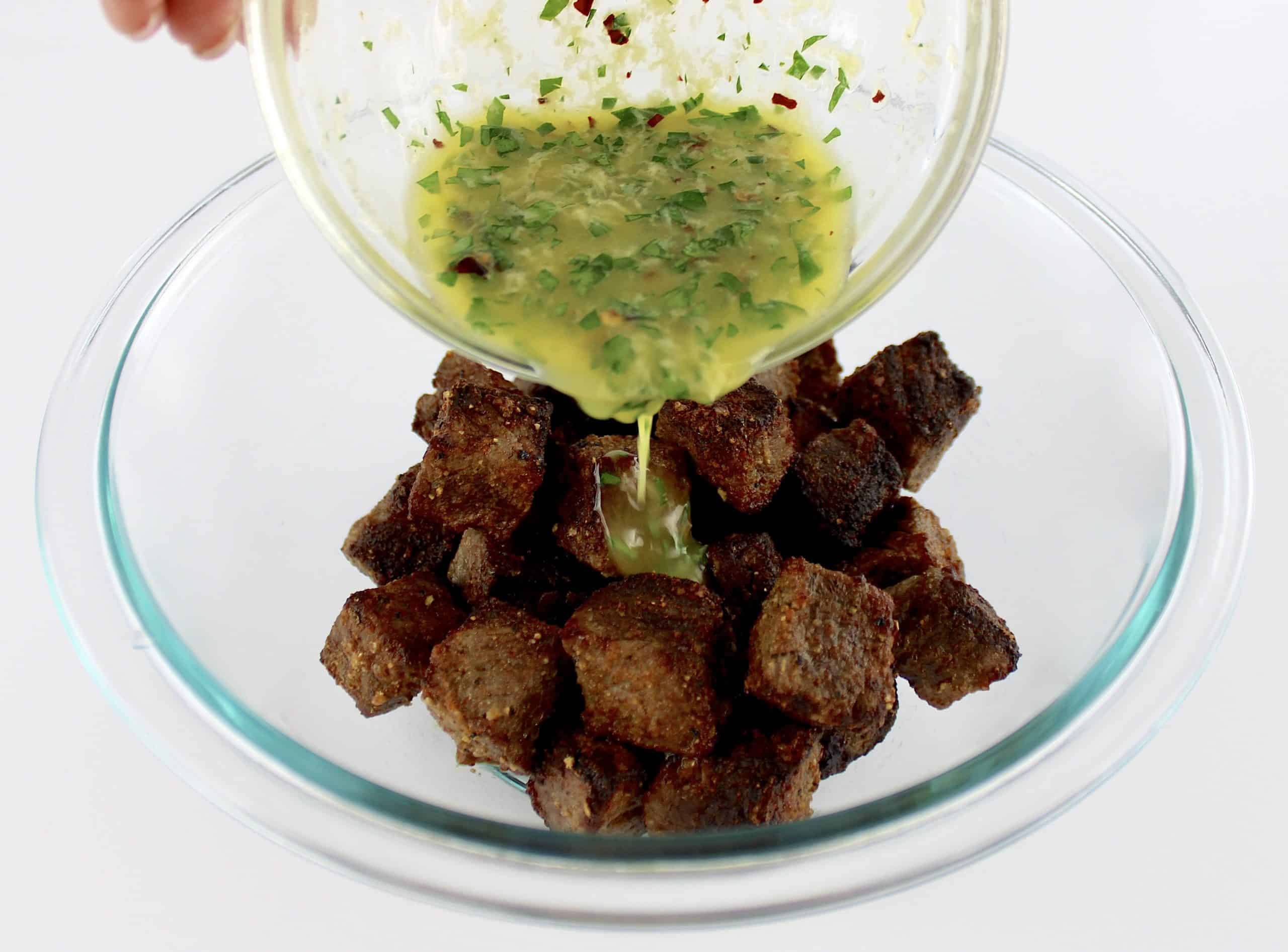 garlic herb butter being poured over steak bites in glass bowl