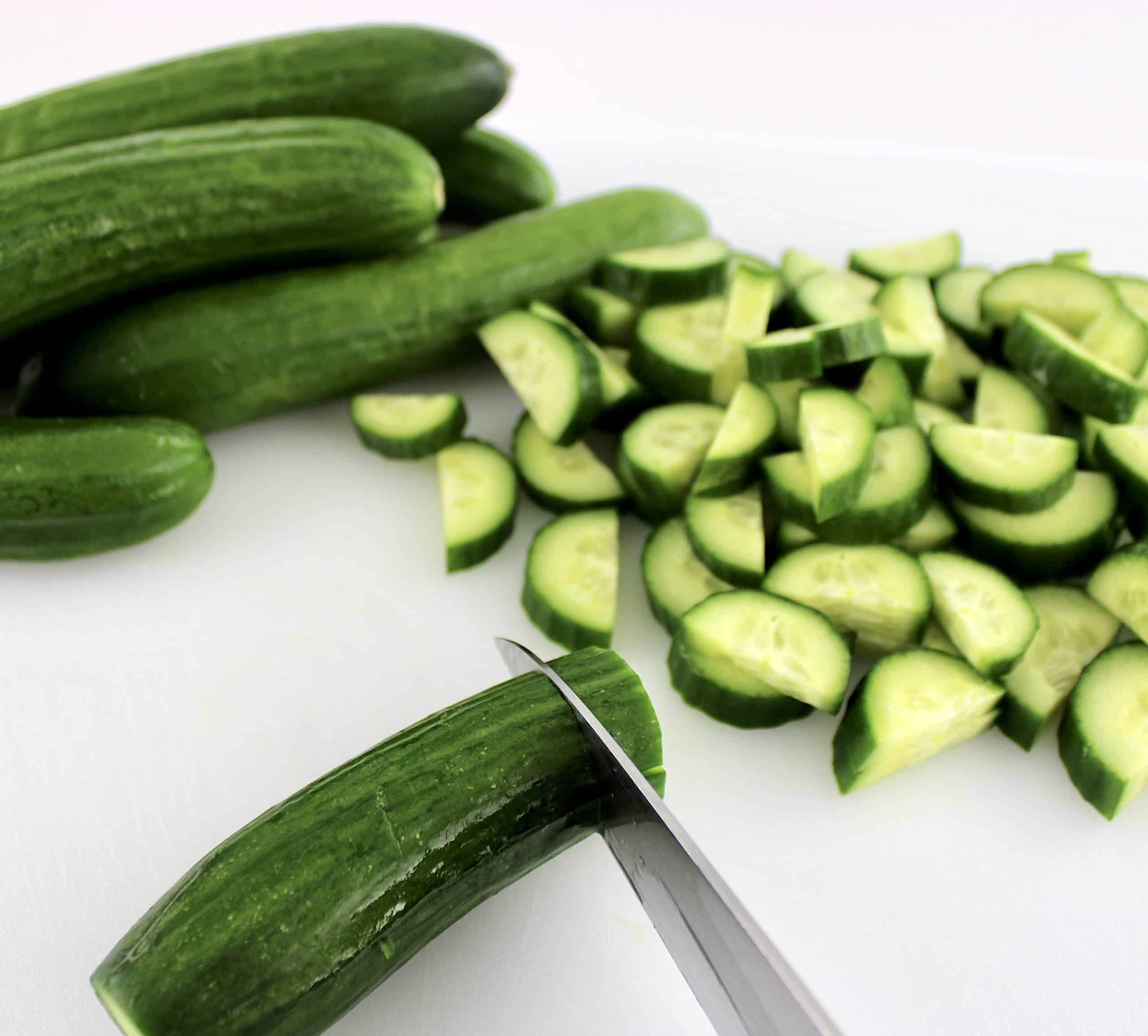 baby cucumbers being sliced on white cutting board