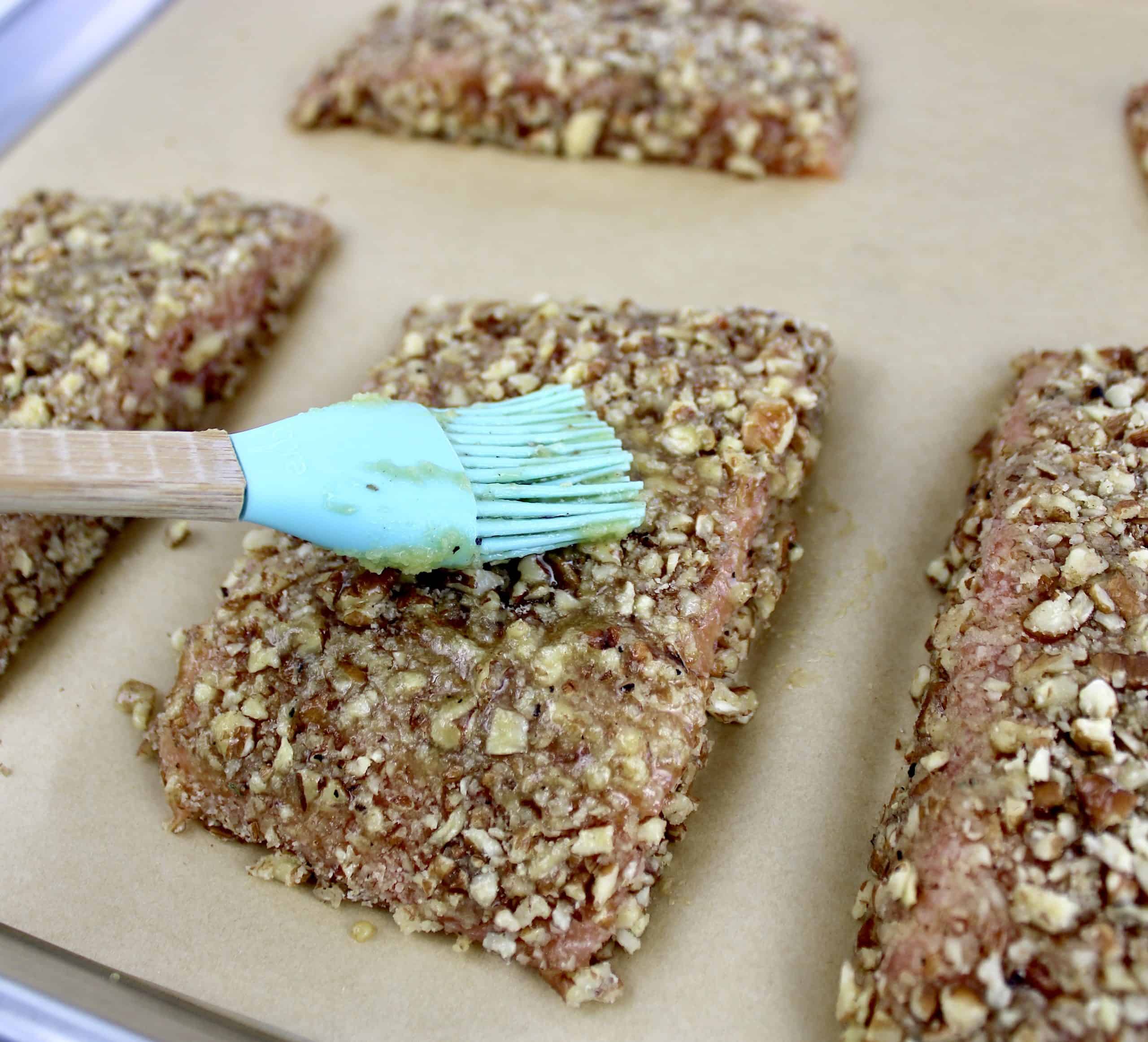 pecan coating with silicone brush over salmon on parchment lined baking sheet