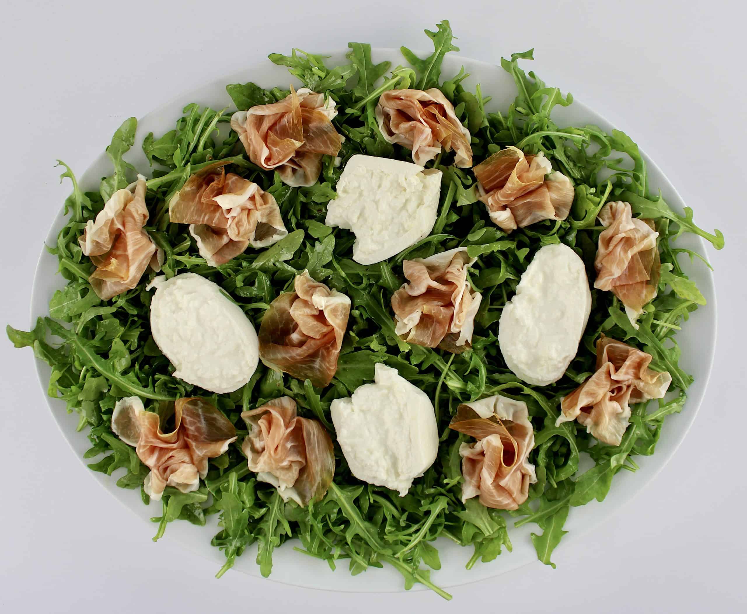 arugula 4 pieces of burrata and bundles of prosciutto on white platter