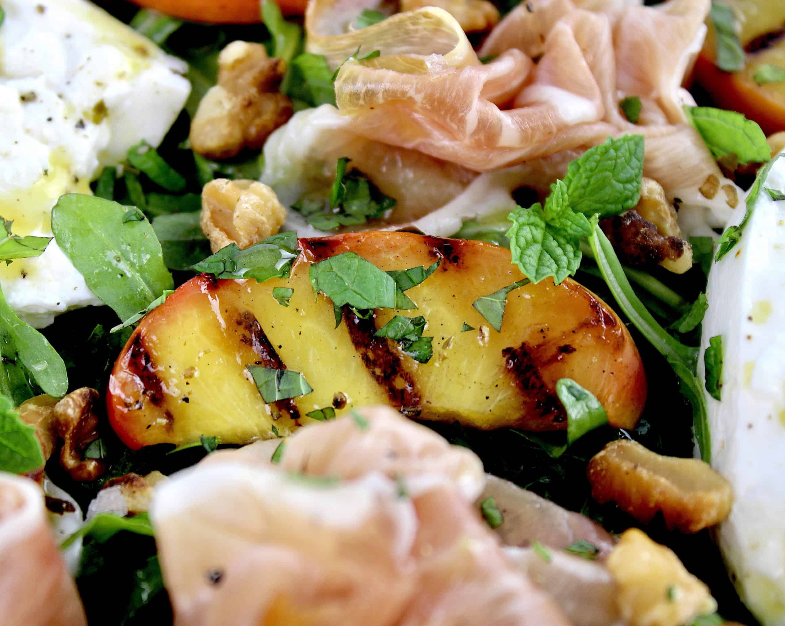 closeup of grilled peach in burrata salad with prosciutto 