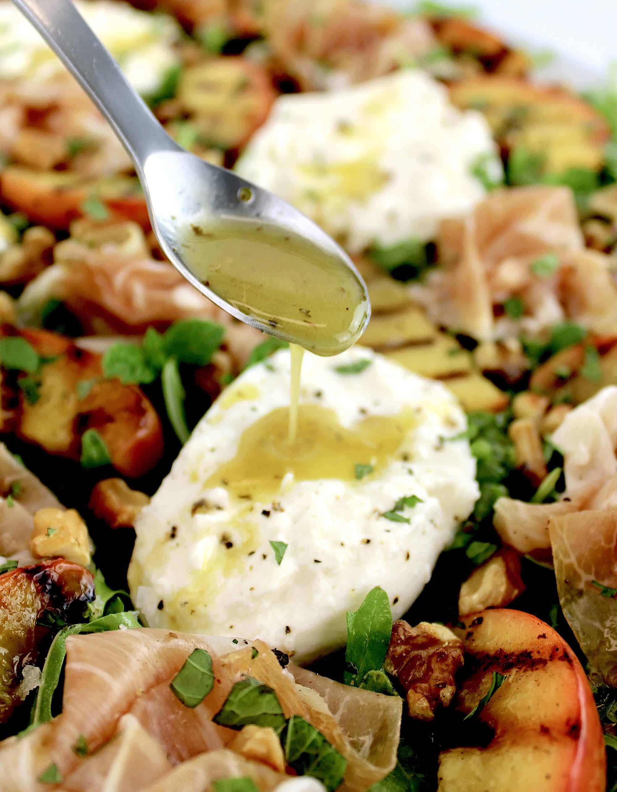 dressing being spooned over piece of burrata in salad with grilled peaches