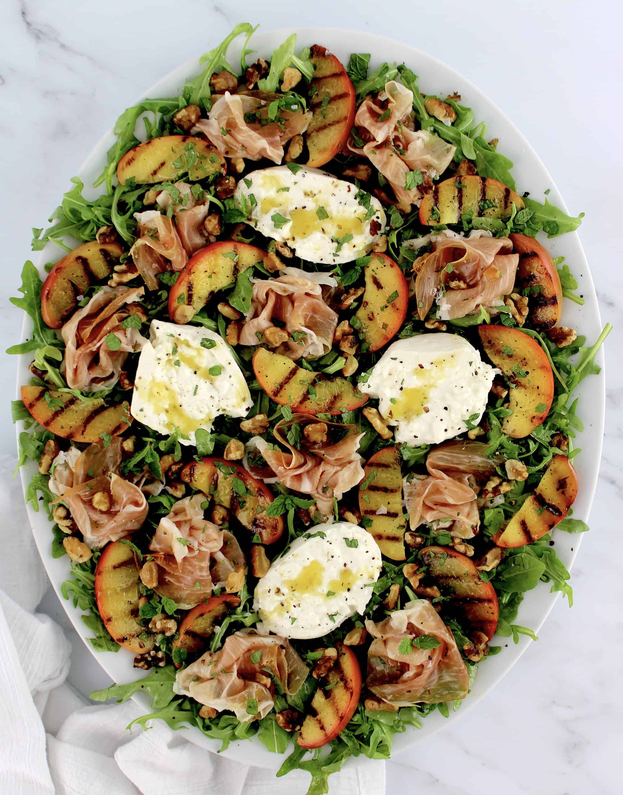overhead view of Grilled Peach Burrata Salad with Prosciutto on white platter