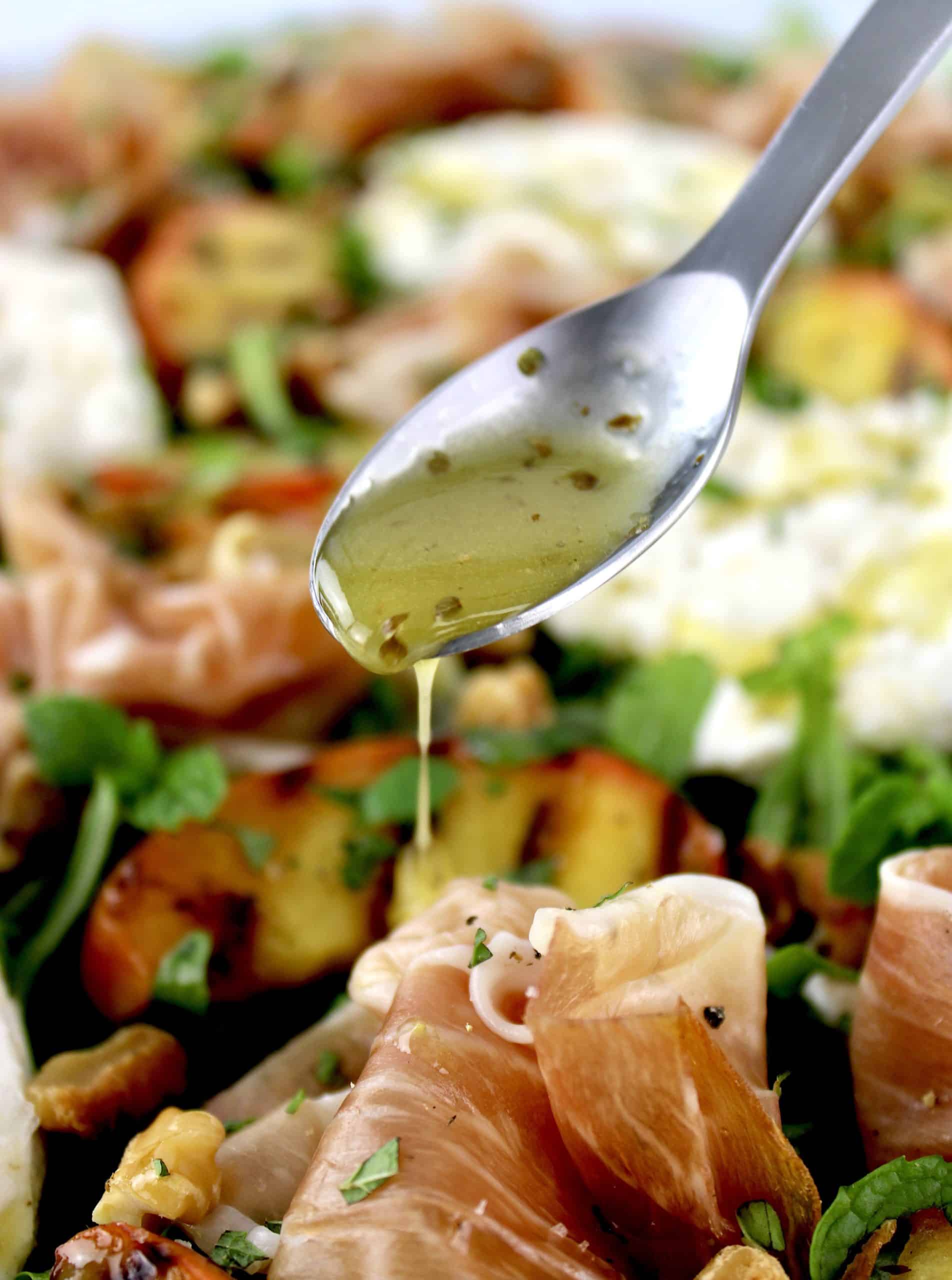 closeup of Grilled Peach Burrata Salad with dressing being spooned over Prosciutto